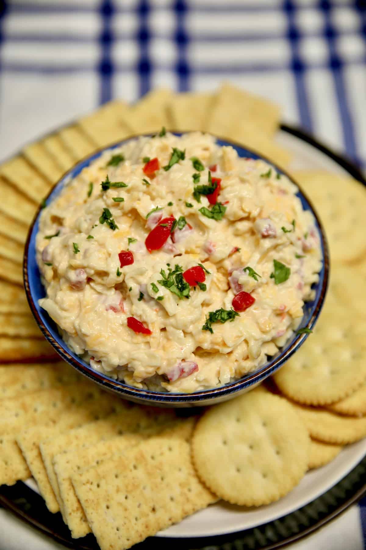 Bowl of pimento cheese on a plate of crackers.