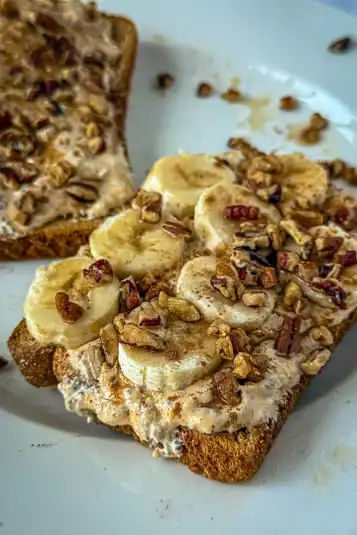 A slice of toast topped with sliced banana, whipped pumpkin and cottage cheese, chopped pecans, and a drizzle of maple syrup on a white plate.
