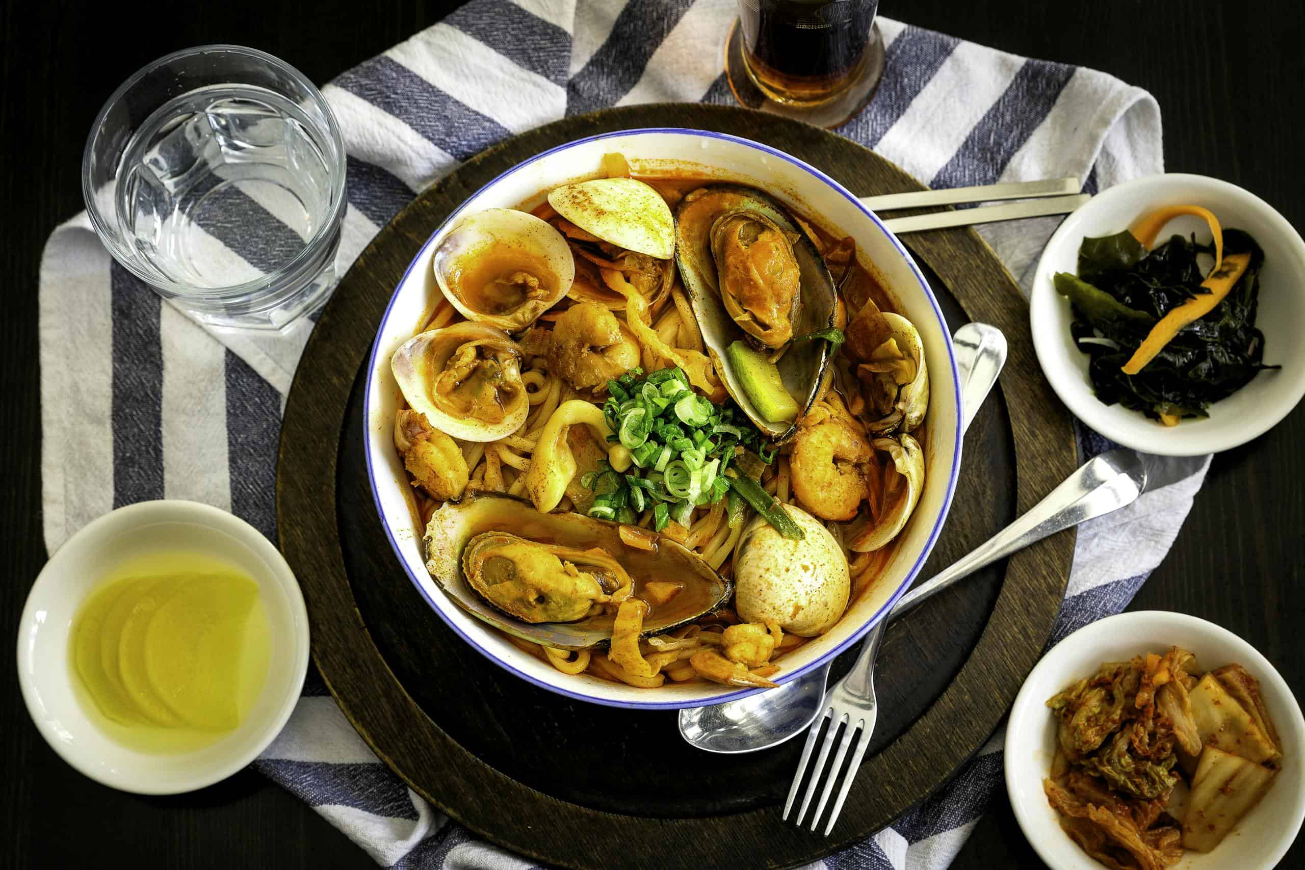 A vibrant Korean seafood noodle dish with side dishes, perfect for a hearty meal.