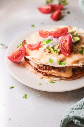The finished taco lasagna topped with sliced tomatoes, parsley and served on a white plate.