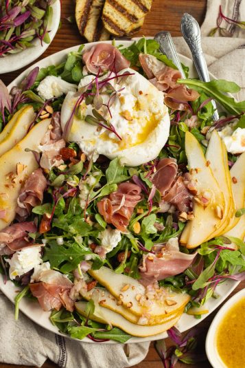This is a picture of a plate filled with an arugula burrata salad with prosciutto and pear.