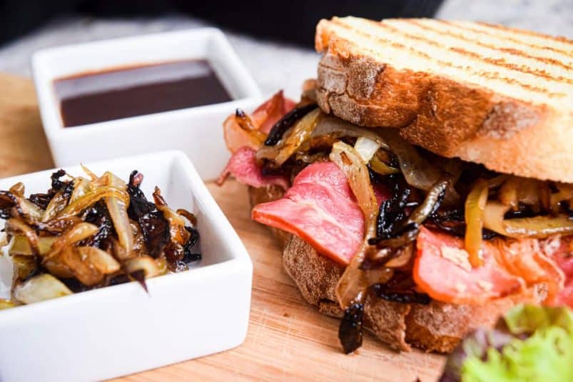 Bacon sandwich on board with caramelized onions and sauce.