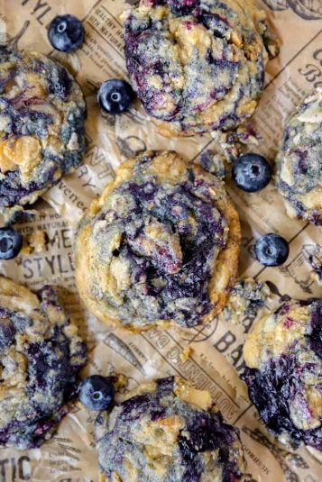 Overhead photo of the blueberry pie cookies with scattered blueberries on brown newsprint paper.