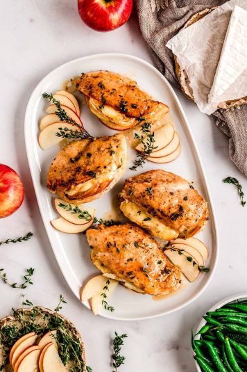 Apple brie stuffed chicken breasts on a white platter, garnished with sliced apples.