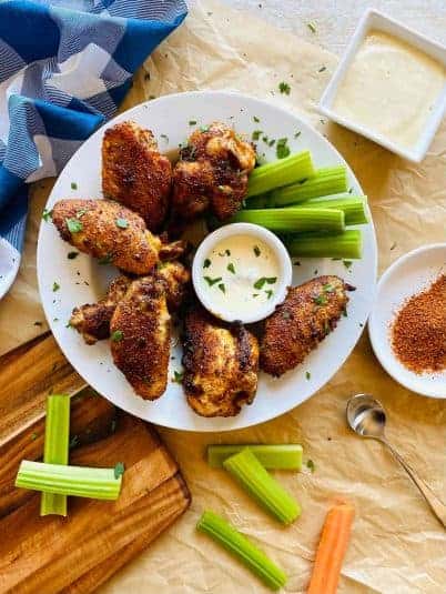 Cajun wings on a plate with dish of blue cheese, celery and carrots.