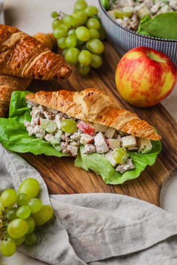 Chicken salad croissant sandwich with lettuce and rotisserie chicken served on a wood board for a healthy lunch.