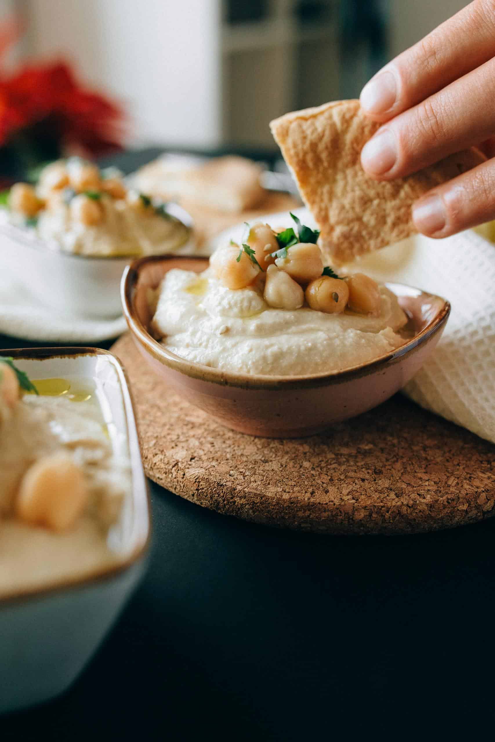 Close-up of a hand dipping pita bread into creamy hummus topped with chickpeas.
