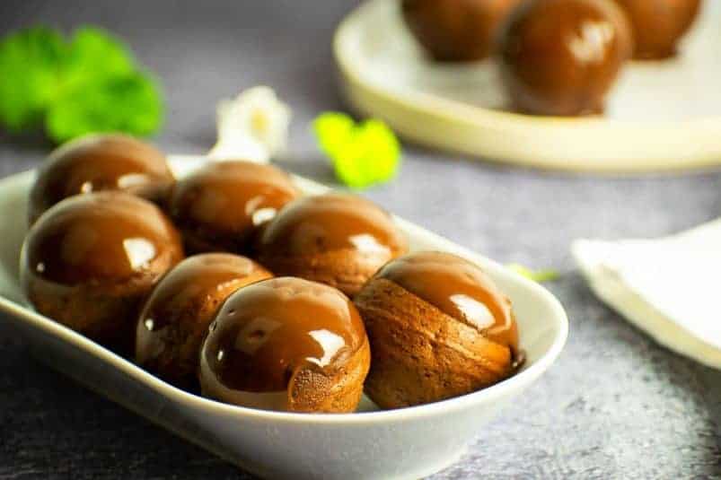 Chocolate covered donut holes on white serving dish.