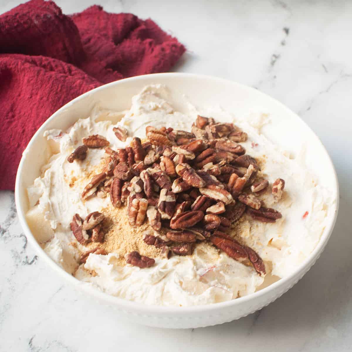 Fall Cheesecake Fruit Salad in a white bowl with a red linen behind it.