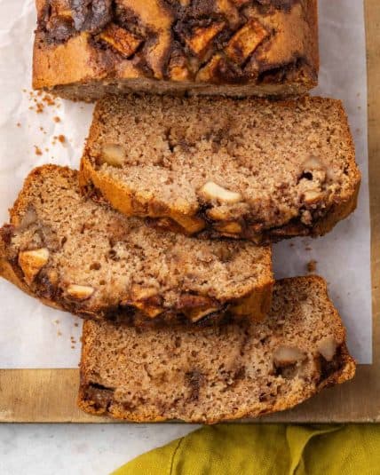 A loaf of gluten free apple bread cut into slices sitting on a wooden board.