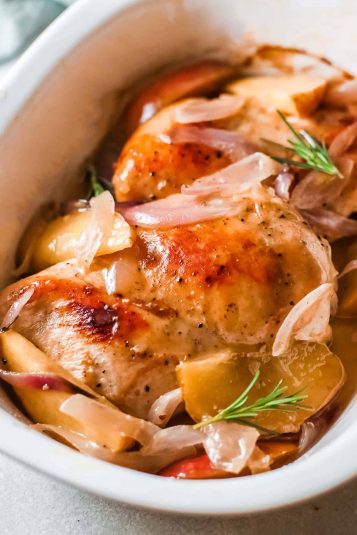 Roast Chicken with Apples and onions in a white baking dish close up.