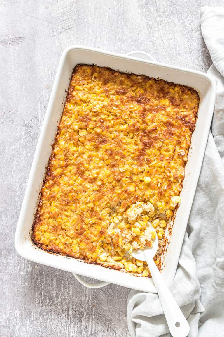 The cooked scalloped corn casserole inside a baking dish with a spoon removing a portion.