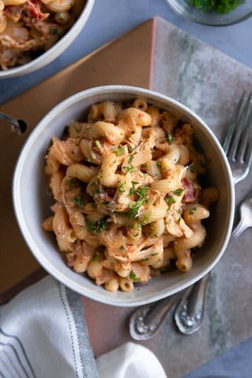 White bowl filled with creamy chicken pasta garnished with parsley.
