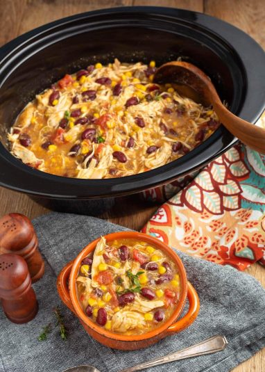 Crock and bowl of soup with linens and wood spoon.