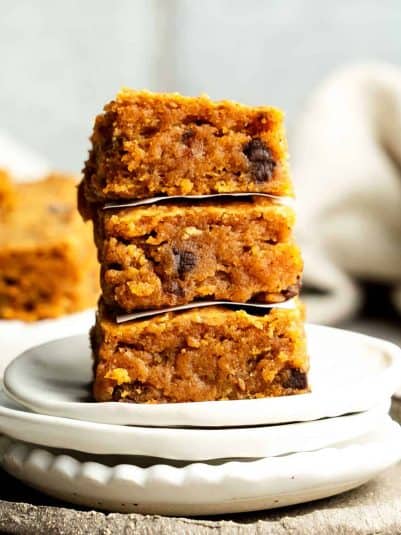Sweet potato blondies stacked three high with parchment between each on two stacked white plates.