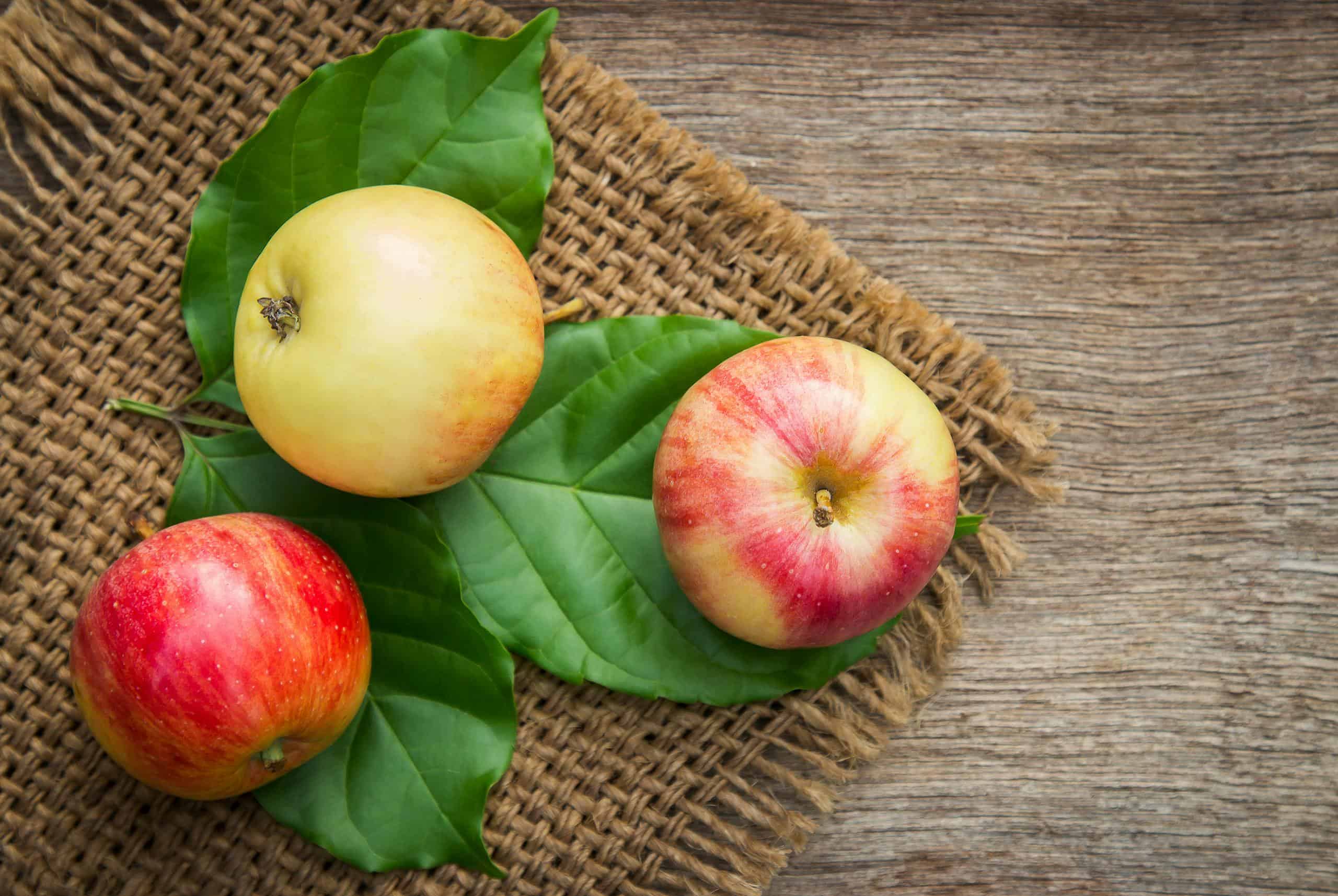 Three ripe apples on leaves over a rustic wooden background, emphasizing freshness and nutrition.