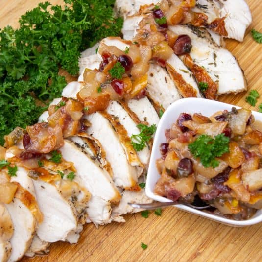 Sliced roast turkey with pear chutney on cutting board with parsley and chutney on the side.