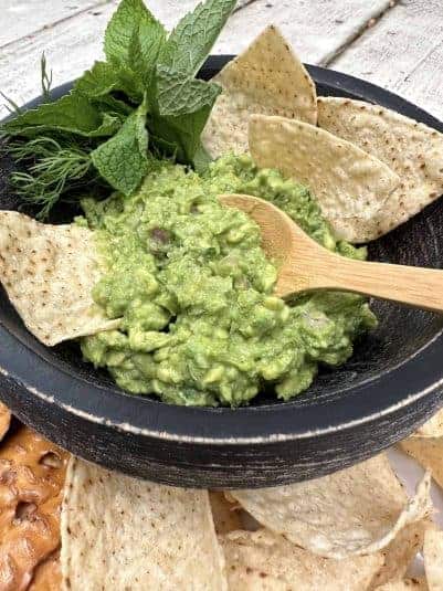 Fresh guacamole in a bowl with chips, fresh herbs and a small spoon dishing up a portion.