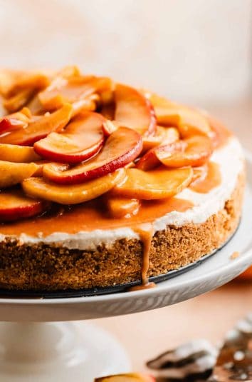 Caramel apple cheesecake on white cake stand with caramel dripping off the side.
