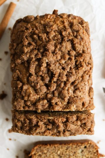 Loaf of cinnamon crunch banana bread partially sliced on parchment paper.