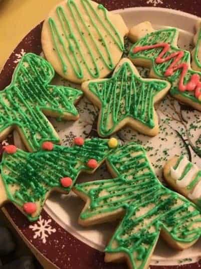 Four peanut butter cookies on a white doily-patterned plate, with a pink cloth in the background on a wooden surface.