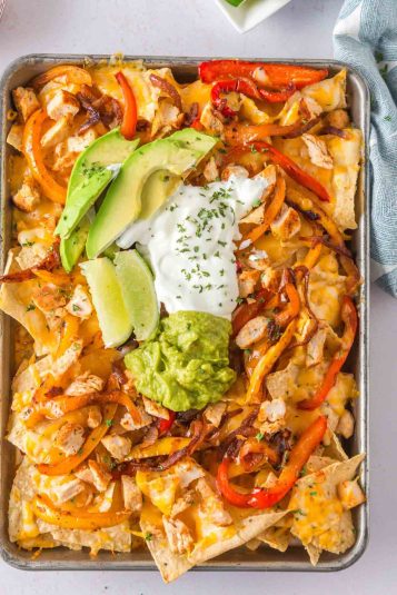 Fajita nachos with chicken and nacho toppings on a baking sheet.