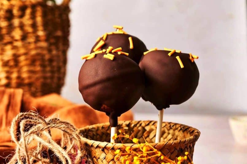 Pumpkin cake pops with orange candy sprinkles in small basket.