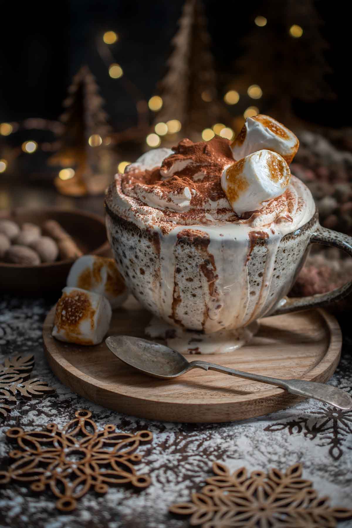 Christmas hot chocolate on a wooden plate with christmas lights in the background.