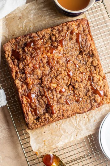 Apple cider coffee cake cooling on a wire rack with a container of caramel in the background.