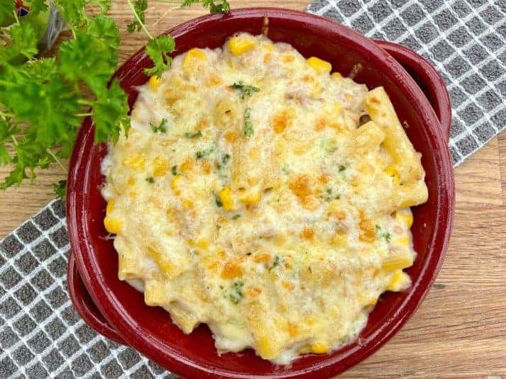 Tuna and sweetcorn pasta in red dish on checked cloth with parsley.