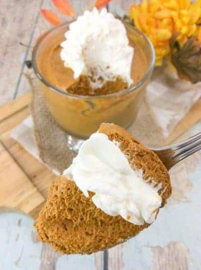 a fork with a bite of airy pumpkin mousse and whipped cream with a trifle dish below.