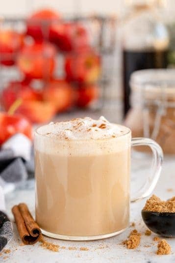 Apple Cider Brown Sugar Latte is served in a glass much. The foamy milk on top is dusted with ground cinnamon.