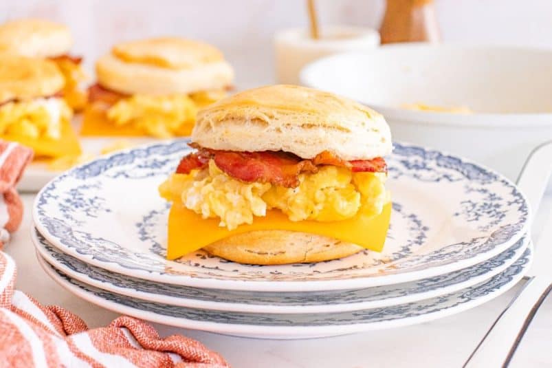 Biscuit breakfast sandwiches with scrambled eggs, cheddar cheese, and bacon are served on a blue-patterned plate.