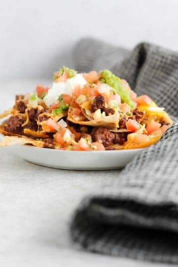 A plate filled with ground bison nachos and topped with sour cream, guacamole, and pico de gallo.