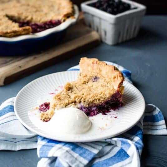 Three blackberry pots de creme lined up on a wooden board next to silver spoons.