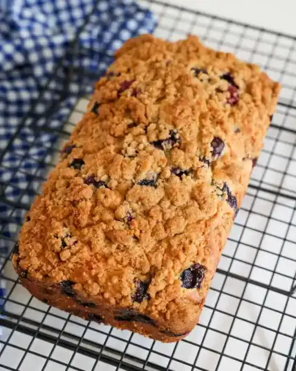 A loaf of blueberry bread cooling on a wire rack.