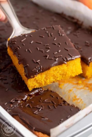 A square piece of carrot cake with chocolate frosting lifted out of the pan.