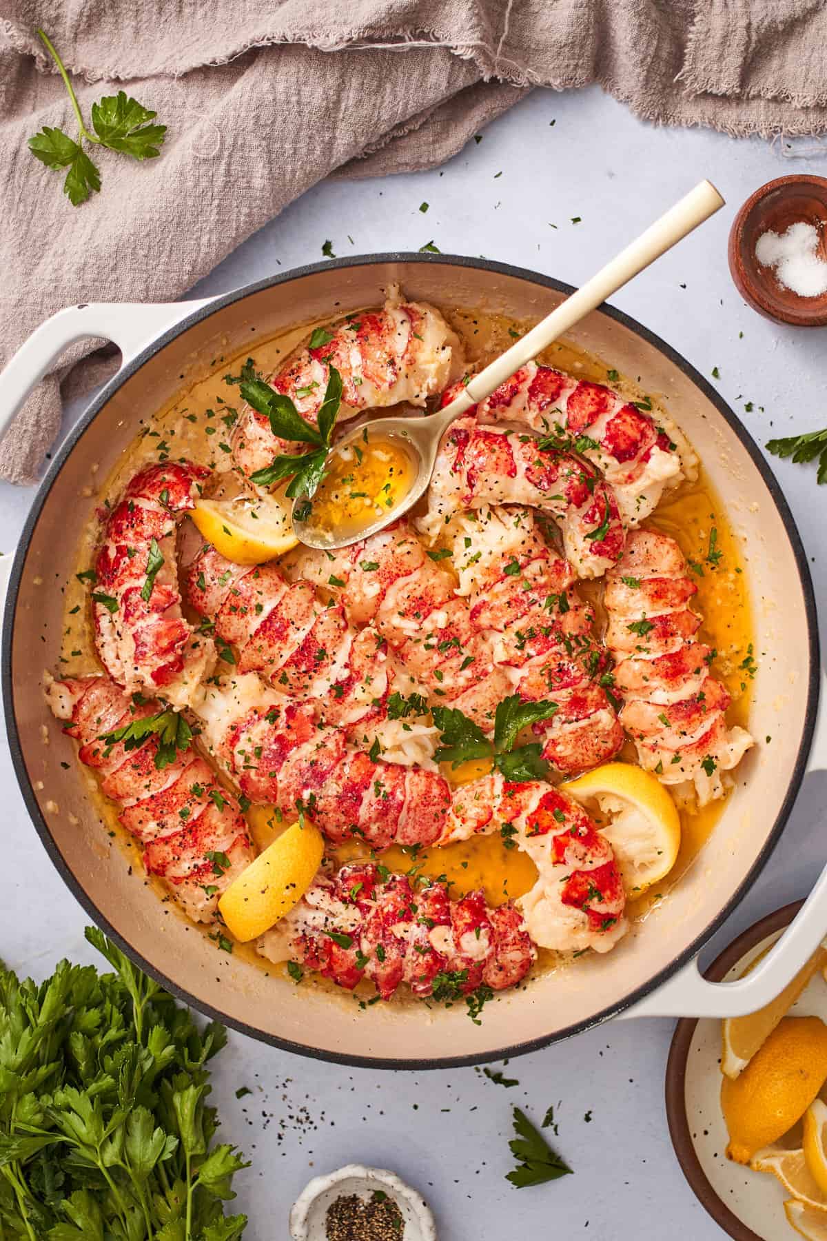 Butter poached lobster tails in an enameled cast iron skillet, with lemon wedges, and parsley.