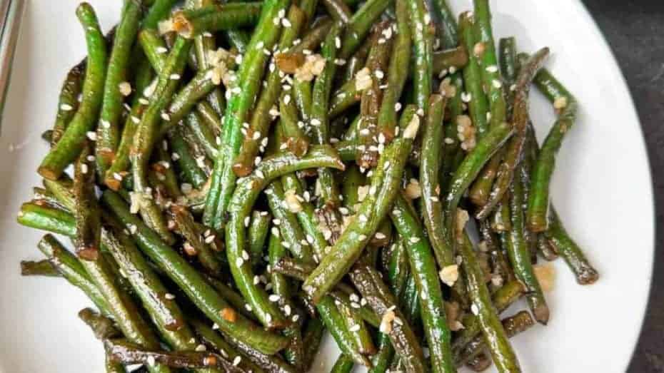 A plate of stir-fried green beans garnished with sesame seeds and minced garlic.