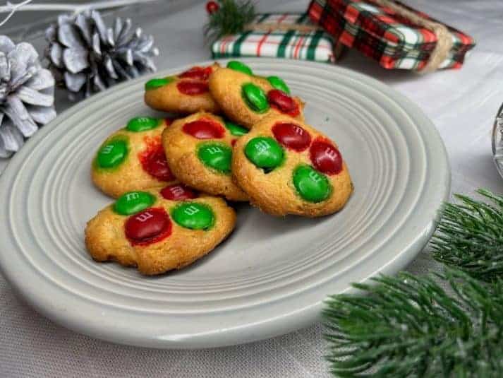 Three cookies with chocolate centers on a red plate, surrounded by festive decorations including pinecones and wrapped gifts.