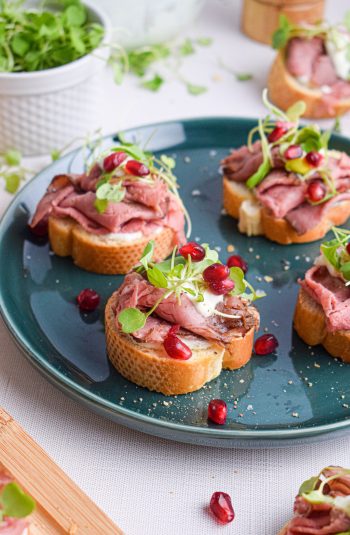 Green plate with crostini topped with roast beef, horseradish sauce, micro arugula and pomegranate seeds.