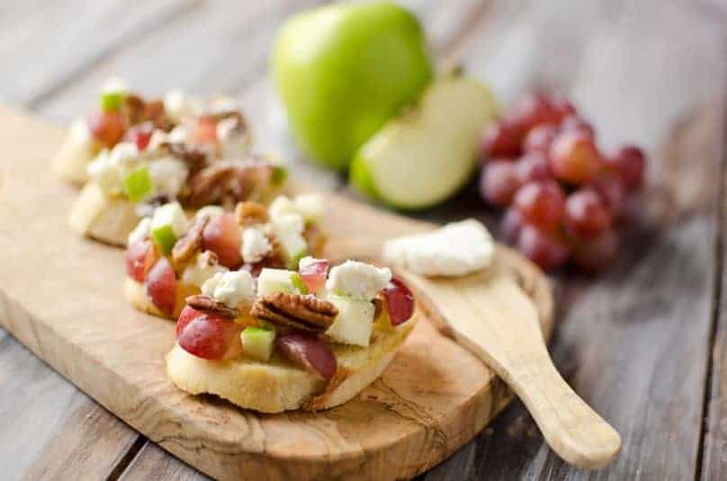 A serving board with roasted grapes phyllo cup appetizers. A plate of appetizers is in the background.
