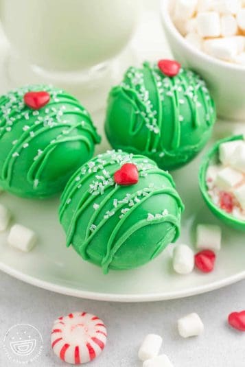 Three green hot chocolate bombs with heart sprinkles on them for grinch theme.