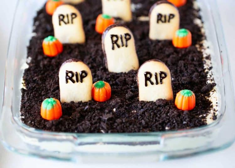 Overhead view of Halloween dirt cake decorated with Oreo “dirt,” cookie tombstones, and candy pumpkins arranged like a graveyard.