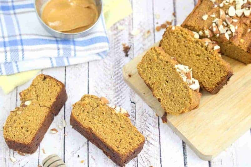 Healthy pumpkin bread in slices on a cutting board and around it with peanut butter on the side.