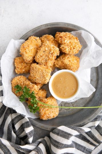 Small tray lined with parchment paper and filled with homemade baked chicken nuggets with a side of honey mustard sauce for dipping.