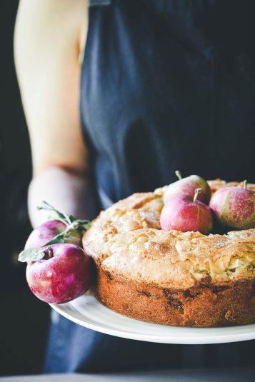 Holding a Jewish cardamom apple cake on a platter with fresh apples.