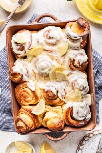 A white pan of baked overnight cinnamon rolls topped with cream cheese frosting.