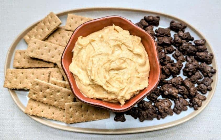 Pumpkin Cheesecake Dip in a bowl with Graham crackers and chocolate Teddy Grahams beside it on a tray.