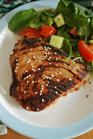 A sliced tuna steak with salad on a white plate.